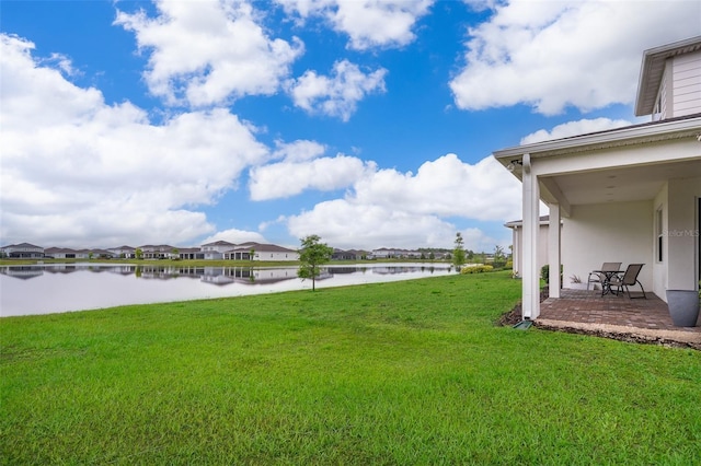 view of green lawn featuring a water view, a residential view, and a patio
