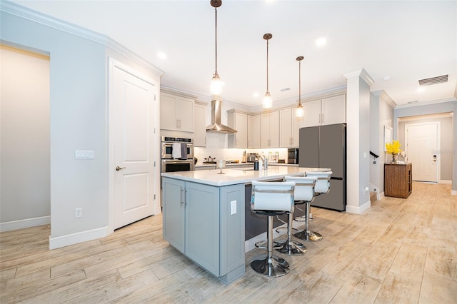 kitchen featuring appliances with stainless steel finishes, wall chimney range hood, light wood-style floors, baseboards, and a kitchen bar