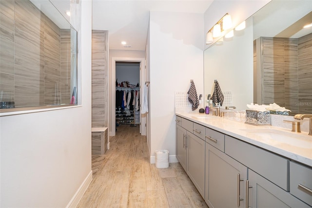 bathroom featuring wood finished floors, double vanity, a walk in closet, recessed lighting, and baseboards