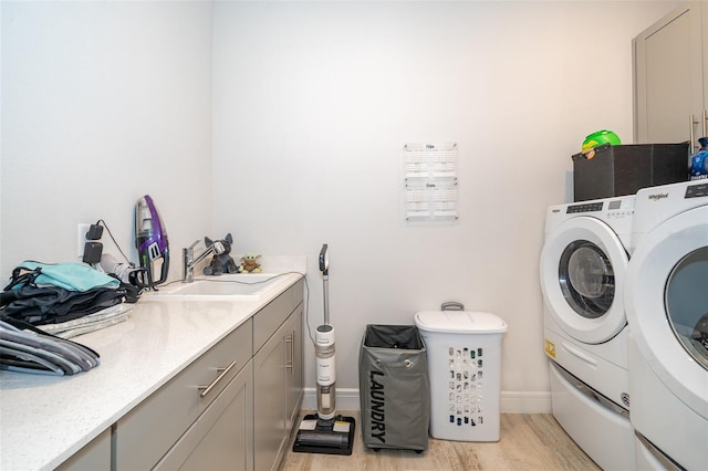 laundry area with washing machine and dryer, light wood-type flooring, cabinet space, and baseboards