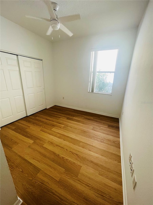 unfurnished bedroom with wood finished floors, a closet, baseboards, and ceiling fan
