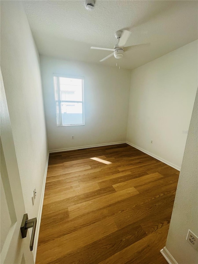 unfurnished room with wood finished floors, a ceiling fan, baseboards, a smoke detector, and a textured ceiling