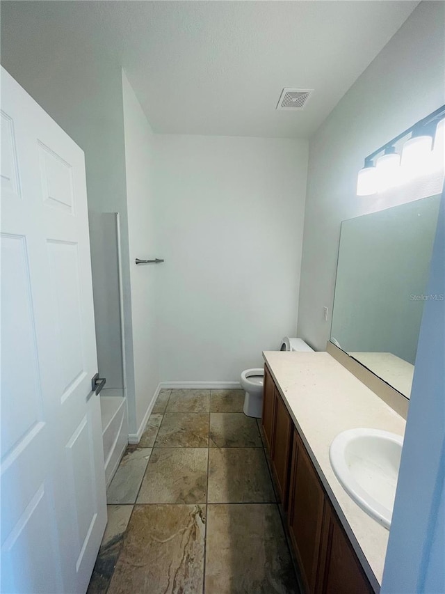 full bath featuring vanity, baseboards, toilet, and stone finish flooring