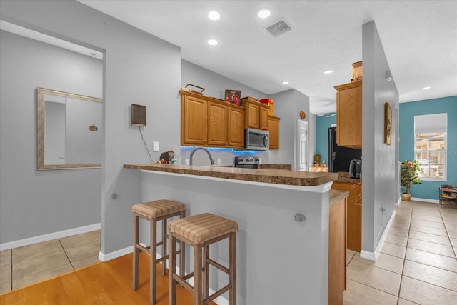 4981 Alita Ter, Saint Cloud, FL 34769 - kitchen with appliances with stainless steel finishes, a breakfast bar, a peninsula, brown cabinetry, and light tile patterned floors
