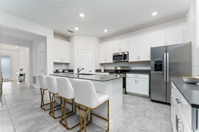 kitchen with appliances with stainless steel finishes, dark countertops, a breakfast bar, white cabinetry, and a sink