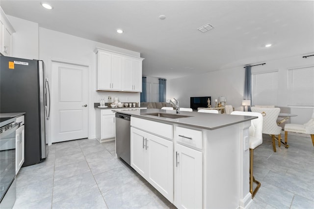kitchen with appliances with stainless steel finishes, a sink, open floor plan, a center island with sink, and white cabinetry