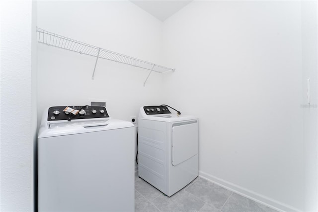 clothes washing area featuring independent washer and dryer, light tile patterned floors, and baseboards