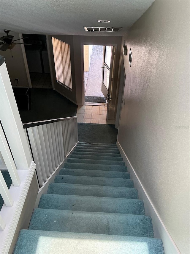 stairway with a textured wall, a ceiling fan, tile patterned flooring, and a textured ceiling