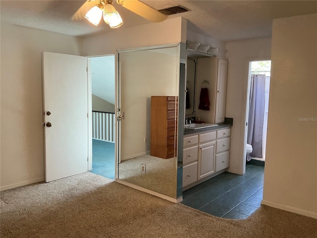 unfurnished bedroom with dark colored carpet, a sink, baseboards, ensuite bathroom, and ceiling fan