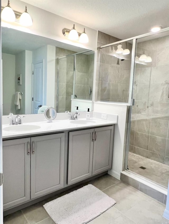 bathroom featuring a shower stall, double vanity, tile patterned floors, and a textured ceiling