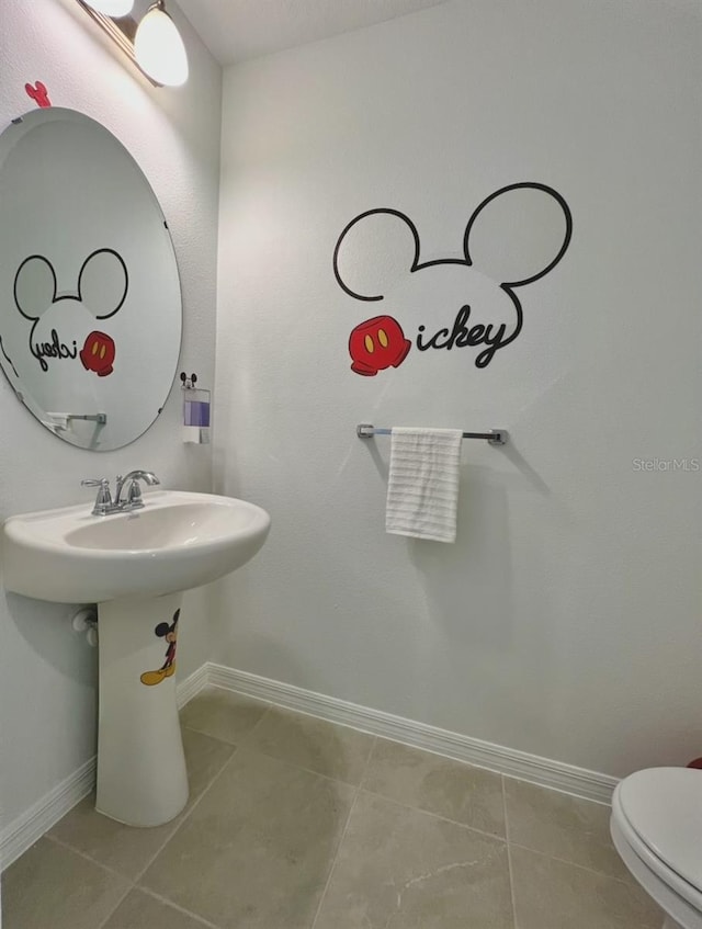 half bath featuring baseboards, tile patterned flooring, and toilet