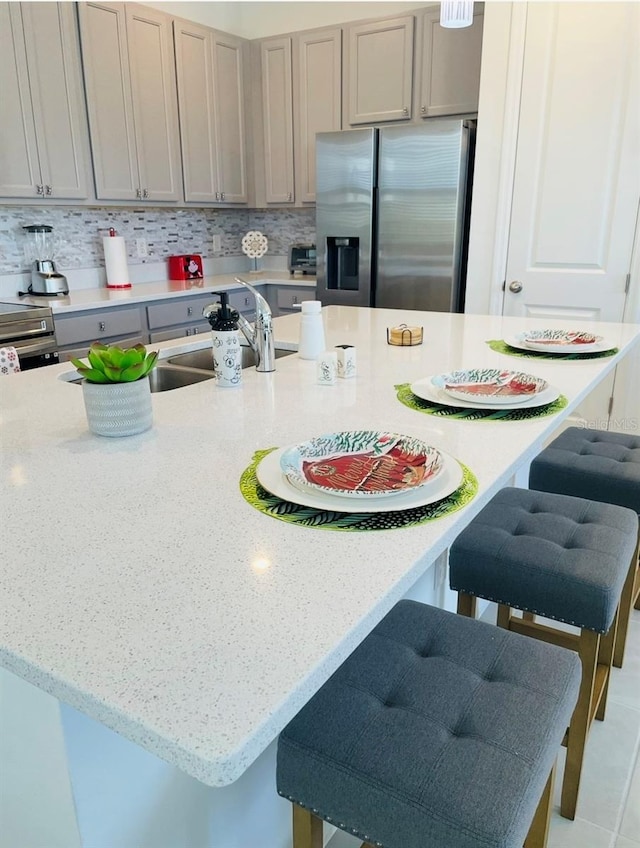 kitchen featuring stainless steel fridge, a sink, a kitchen bar, gray cabinets, and light stone counters