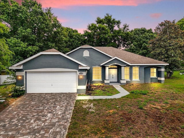 ranch-style home featuring decorative driveway, a garage, stucco siding, and a yard