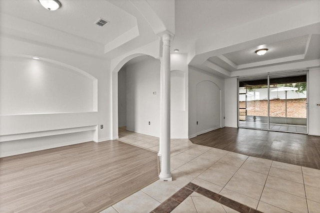 spare room featuring a tray ceiling, tile patterned flooring, baseboards, and arched walkways