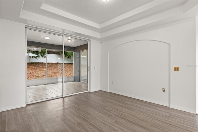 unfurnished room with wood finished floors, baseboards, and a tray ceiling