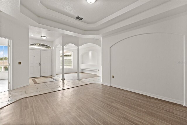 foyer with arched walkways, decorative columns, wood finished floors, a raised ceiling, and baseboards