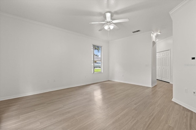 spare room featuring ceiling fan, ornamental molding, light wood-type flooring, baseboards, and arched walkways