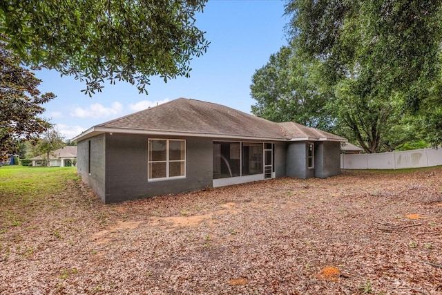 rear view of house with fence, stucco siding, roof with shingles, and a sunroom