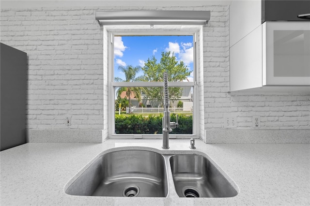 3203 Herons Point Cir, Kissimmee, FL 34741 - kitchen view of a sink, brick wall, white cabinetry, glass insert cabinets, and light stone countertops