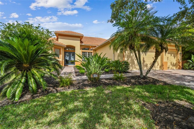 517 Milano Rd, Poinciana, FL 34759 - mediterranean / spanish-style house featuring french doors, stucco siding, a garage, a tiled roof, and decorative driveway