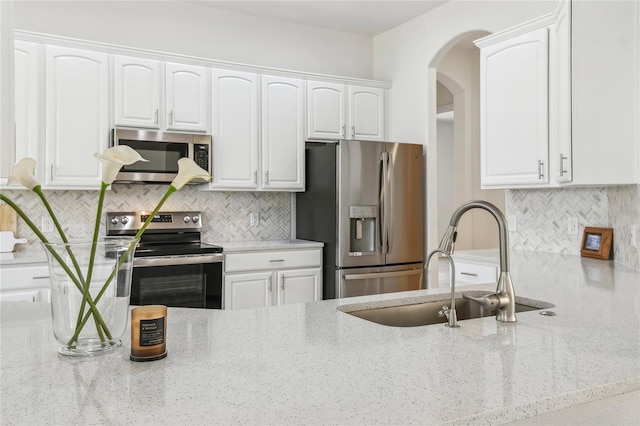 517 Milano Rd, Poinciana, FL 34759 - kitchen featuring stainless steel appliances, arched walkways, light stone countertops, white cabinets, and decorative backsplash
