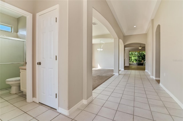corridor featuring arched walkways, light tile patterned floors, and baseboards