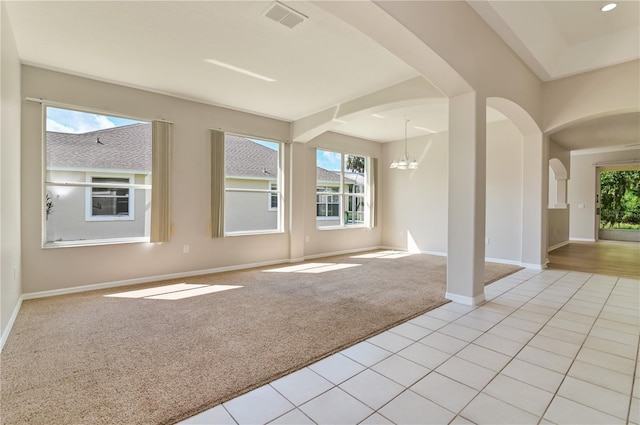 empty room with light colored carpet, arched walkways, a chandelier, and baseboards