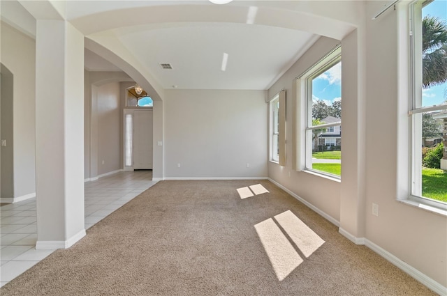 spare room with arched walkways, light carpet, light tile patterned floors, and healthy amount of natural light