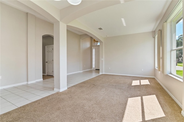 carpeted spare room featuring arched walkways, tile patterned flooring, and baseboards
