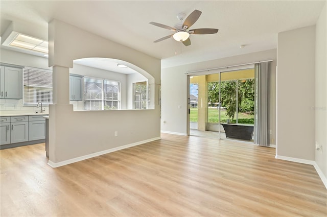 empty room featuring light wood-style flooring, a sink, ceiling fan, baseboards, and arched walkways