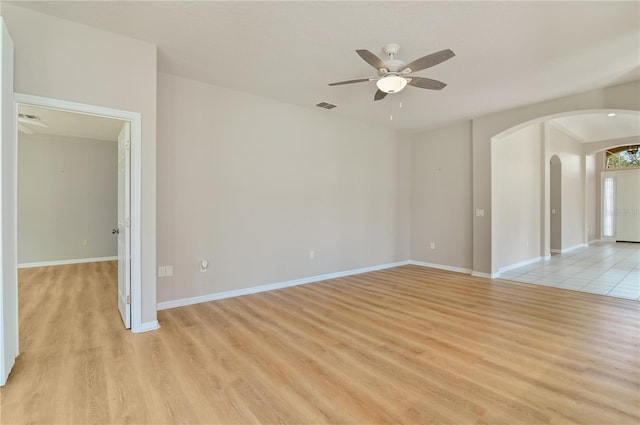 unfurnished room featuring arched walkways, a ceiling fan, light wood finished floors, and baseboards