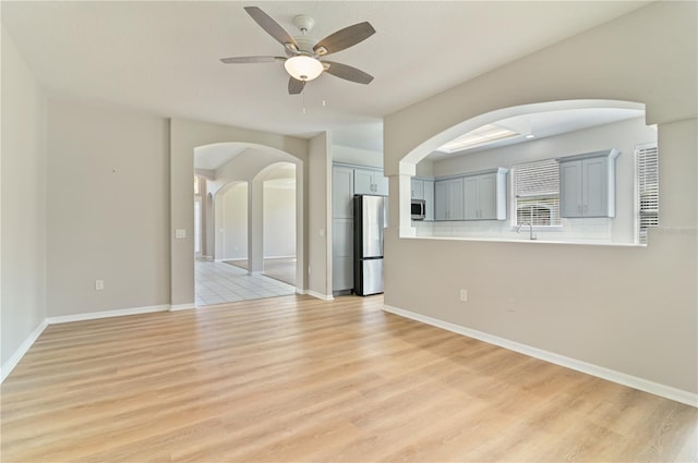 unfurnished living room featuring light wood finished floors, ceiling fan, arched walkways, and baseboards