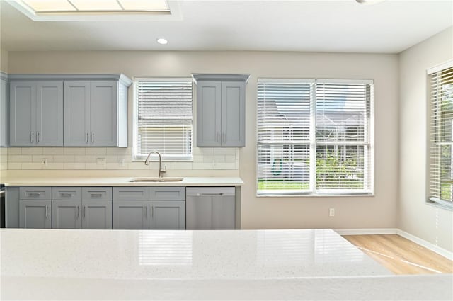 kitchen with a sink, stainless steel dishwasher, gray cabinetry, light wood-type flooring, and baseboards