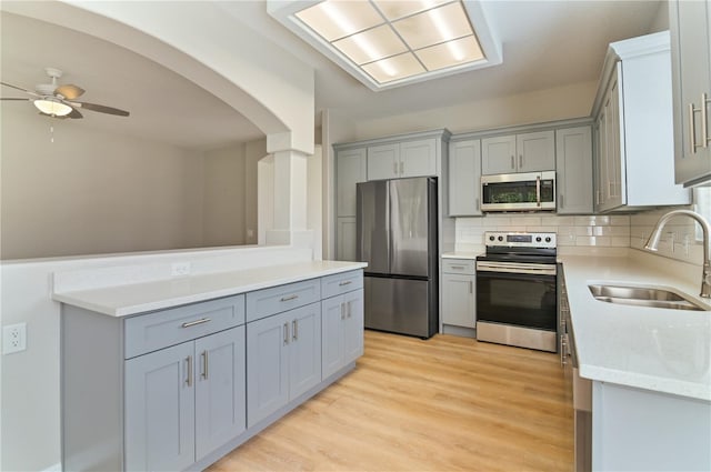 kitchen featuring stainless steel appliances, a sink, gray cabinetry, and a ceiling fan