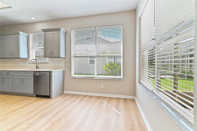 kitchen featuring gray cabinetry, dishwasher, light wood-style flooring, backsplash, and plenty of natural light