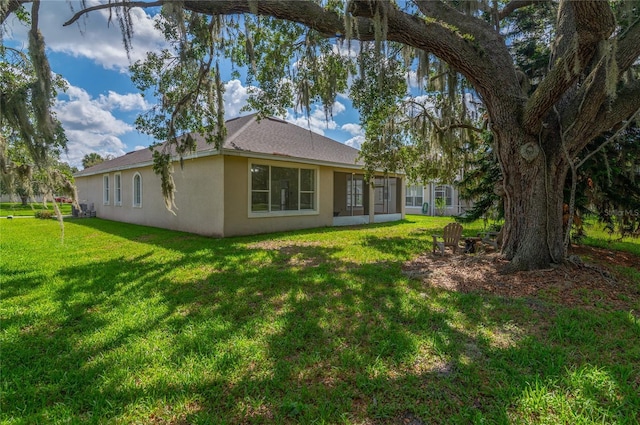 back of property featuring stucco siding, a lawn, and roof with shingles