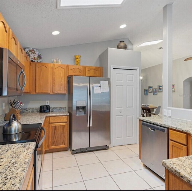 2567 Oneida Loop, Kissimmee, FL 34747 - kitchen featuring appliances with stainless steel finishes, light tile patterned flooring, light stone counters, a textured ceiling, and brown cabinets