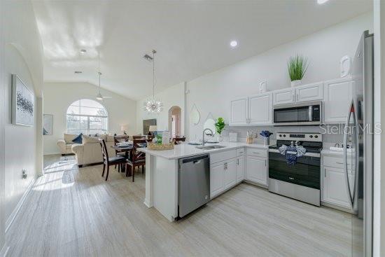 926 Balmoral Dr, Davenport, FL 33896 - kitchen with stainless steel appliances, a sink, lofted ceiling, a peninsula, and light wood finished floors