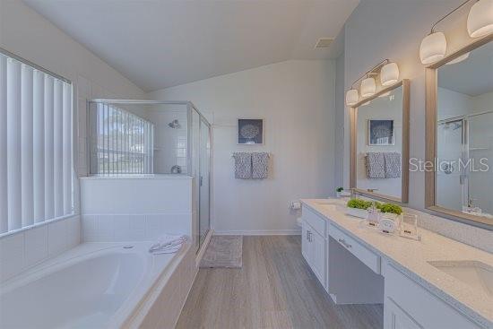 926 Balmoral Dr, Davenport, FL 33896 - bathroom with vaulted ceiling, a stall shower, double vanity, a garden tub, and wood finished floors