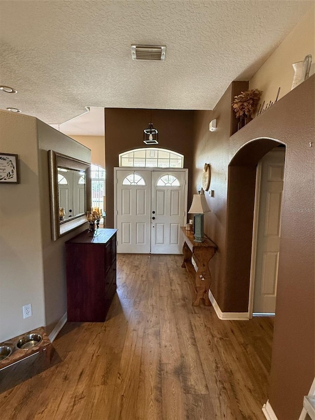 foyer featuring arched walkways, wood finished floors, a textured ceiling, and baseboards