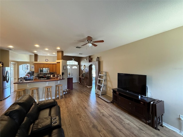 living room with wood finished floors, a ceiling fan, recessed lighting, baseboards, and arched walkways