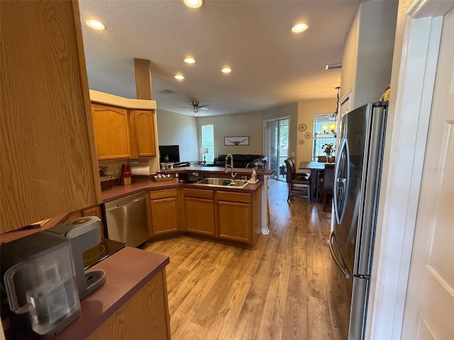 kitchen with a sink, stainless steel appliances, a peninsula, brown cabinetry, and light wood-style flooring