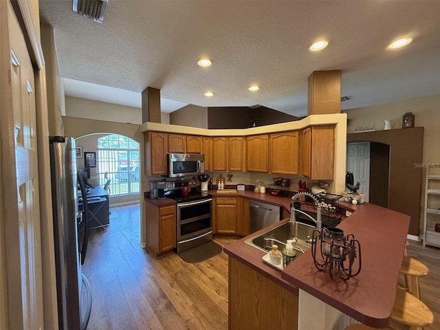 kitchen featuring appliances with stainless steel finishes, arched walkways, a peninsula, light wood-style flooring, and a sink