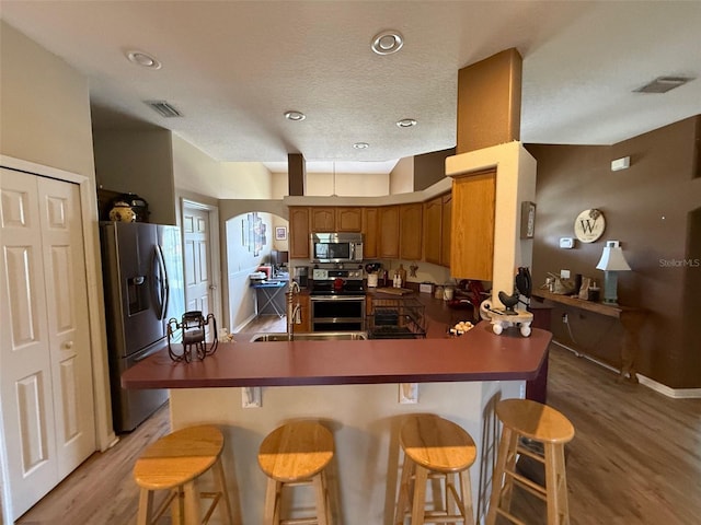 kitchen with stainless steel appliances, a peninsula, light wood-type flooring, brown cabinets, and arched walkways