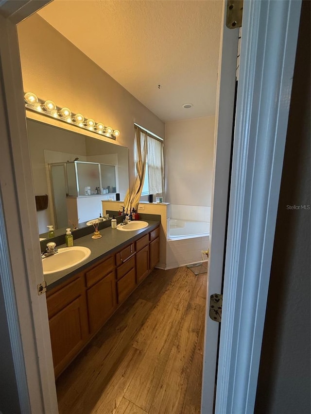 bathroom with wood finished floors, a bath, a stall shower, double vanity, and a textured ceiling