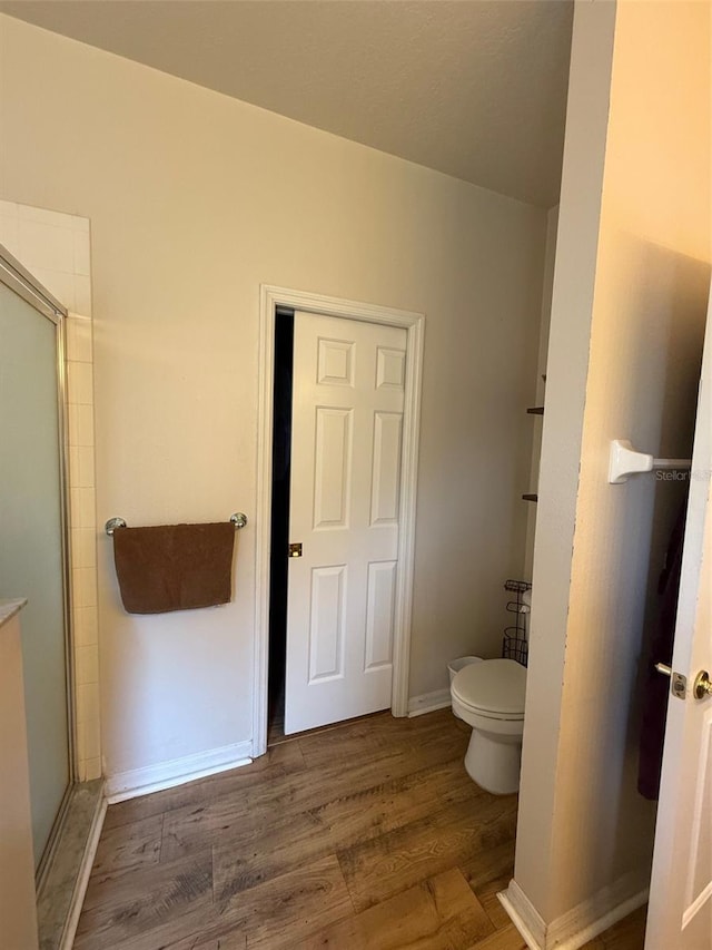 bathroom featuring wood finished floors, toilet, a shower with door, and baseboards