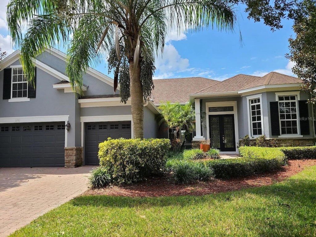 1771 Lee Janzen Dr, Kissimmee, FL 34744 - view of front of property featuring french doors, stucco siding, stone siding, decorative driveway, and a garage