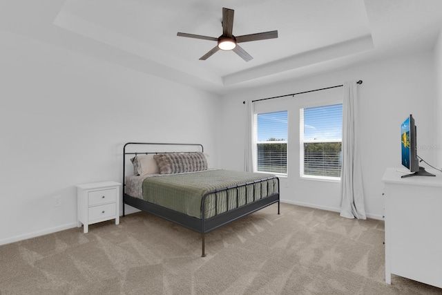 carpeted bedroom with a raised ceiling, baseboards, and a ceiling fan