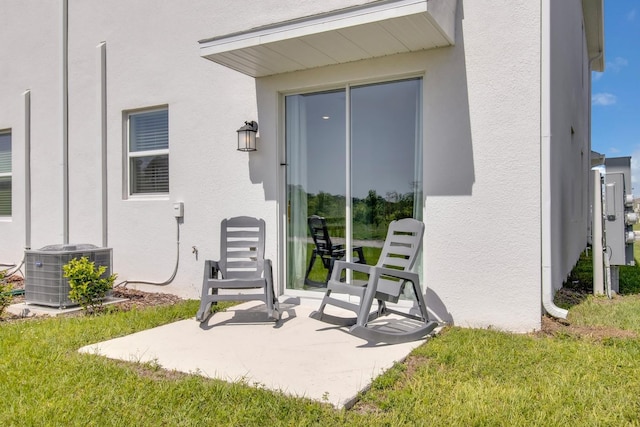 property entrance with central air condition unit, stucco siding, a lawn, and a patio area