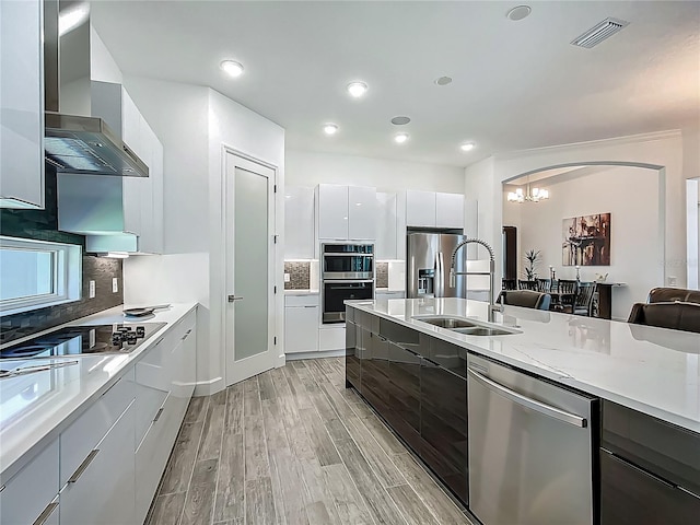 kitchen featuring appliances with stainless steel finishes, modern cabinets, wall chimney exhaust hood, a sink, and light wood-type flooring